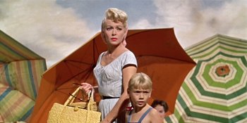 Movie still from “Imitation of Life” (1959), directed by Douglas Sirk – A woman and a boy are standing under an umbrella; Medium shot, Low angle