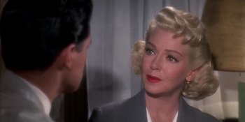 Movie still from “Imitation of Life” (1959), directed by Douglas Sirk – A woman with blonde hair wearing a gray suit and red lipstick; Close Up shot, Over the shoulder angle