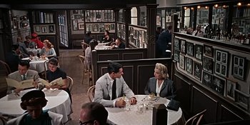 Movie still from “Imitation of Life” (1959), directed by Douglas Sirk – A man and a woman sitting at a table in a restaurant; Wide shot, High angle