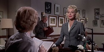Movie still from “Imitation of Life” (1959), directed by Douglas Sirk – A woman in a gray suit standing in front of another woman; Medium shot, Over the shoulder angle