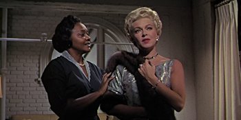 Movie still from “Imitation of Life” (1959), directed by Douglas Sirk – Two women in a room one is holding a fur collar; Medium shot, Low angle