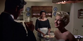 Movie still from “Imitation of Life” (1959), directed by Douglas Sirk – Two women and a man are serving food to one another in a dining room; Medium shot, Over the shoulder angle