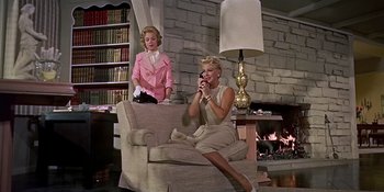 Movie still from “Imitation of Life” (1959), directed by Douglas Sirk – Two women sitting on a couch in front of a fire place; Wide shot, Low angle