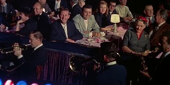 Movie still from “Imitation of Life” (1959), directed by Douglas Sirk – A group of people sitting at a table with a trombone; Medium shot, High angle