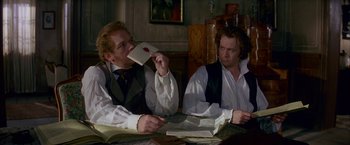 Movie still from “Immortal Beloved” (1994), directed by Bernard Rose – Two men sitting at a table with papers and a book; Medium shot, Over the shoulder angle