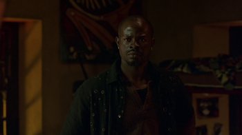 Movie still from “In America” (2002), directed by Jim Sheridan – A man in a black shirt and a black jacket is in a dark room; Medium shot, Low angle