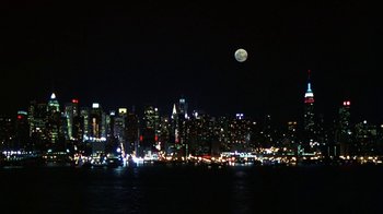 Movie still from “In America” (2002), directed by Jim Sheridan – A view of a city skyline at night with a full moon in the background; Extreme Wide shot, High angle