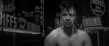 Movie still from “In Cold Blood” (1967), directed by Richard Brooks – A black and white photo of a man in front of a neon sign; Close Up shot, Low angle