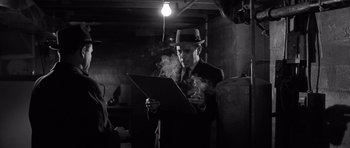 Movie still from “In Cold Blood” (1967), directed by Richard Brooks – A man in a suit and hat is holding a piece of paper; Medium shot, Low angle