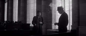 Movie still from “In Cold Blood” (1967), directed by Richard Brooks – A man in a suit and hat smoking a cigarette in front of a mirror; Medium shot, Low angle