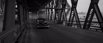 Movie still from “In Cold Blood” (1967), directed by Richard Brooks – An old car driving on a road under a bridge; Extreme Wide shot, High angle