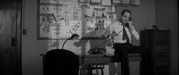 Movie still from “In Cold Blood” (1967), directed by Richard Brooks – A black and white photo of a man sitting at a desk; Medium shot, Low angle