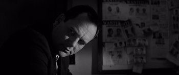 Movie still from “In Cold Blood” (1967), directed by Richard Brooks – A black - and - white photo of a man in front of posters; Close Up shot, Low angle