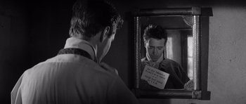 Movie still from “In Cold Blood” (1967), directed by Richard Brooks – A man looking in the mirror while holding a note; Close Up shot, Over the shoulder angle