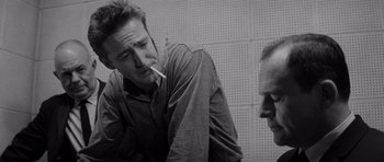 Movie still from “In Cold Blood” (1967), directed by Richard Brooks – A man smoking a cigarette while another man looks on; Close Up shot, Low angle