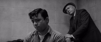 Movie still from “In Cold Blood” (1967), directed by Richard Brooks – A man and another man are sitting in front of a wall; Medium shot, Low angle