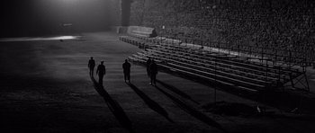 Movie still from “In Cold Blood” (1967), directed by Richard Brooks – A group of people standing in a field near a stadium; Extreme Wide shot, High angle