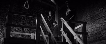 Movie still from “In Cold Blood” (1967), directed by Richard Brooks – A man in a suit standing next to a rope hanging; Wide shot, Low angle
