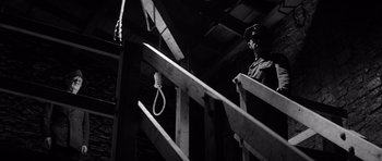 Movie still from “In Cold Blood” (1967), directed by Richard Brooks – A man standing on top of a set of stairs next to a rope; Medium shot, Low angle