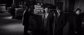 Movie still from “In Cold Blood” (1967), directed by Richard Brooks – Two men in suits and hats standing in a warehouse; Medium shot, Low angle