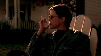 Movie still from “In Dreams” (1999), directed by Neil Jordan – A woman sitting on top of a chair smoking a cigarette; Medium shot, Over the shoulder angle