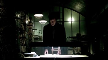 Movie still from “In Dreams” (1999), directed by Neil Jordan – A man standing in front of a desk in a dark room; Medium shot, Low angle