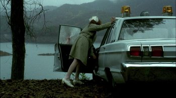 Movie still from “In Dreams” (1999), directed by Neil Jordan – A woman in a trench coat is putting a car in the trunk of a car; Wide shot, High angle
