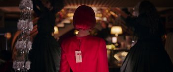 Movie still from “In Fabric” (2018), directed by Peter Strickland – A woman in a red jacket with a price tag on it's back; Medium shot, Over the shoulder angle
