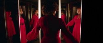 Movie still from “In Fabric” (2018), directed by Peter Strickland – A woman in a red dress is looking in the mirror; Medium shot, Overhead angle