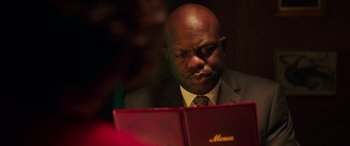 Movie still from “In Fabric” (2018), directed by Peter Strickland – A man sitting at a table looking at a menu; Close Up shot, Over the shoulder angle