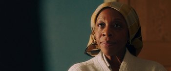 Movie still from “In Fabric” (2018), directed by Peter Strickland – An older woman wearing a head scarf looking at the camera; Close Up shot, Over the shoulder angle