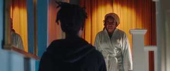 Movie still from “In Fabric” (2018), directed by Peter Strickland – A woman in a bathrobe looking in the mirror; Medium shot, Over the shoulder angle