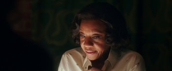 Movie still from “In Fabric” (2018), directed by Peter Strickland – An older woman is smiling while looking at the camera; Close Up shot, Over the shoulder angle