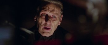 Movie still from “In Fabric” (2018), directed by Peter Strickland – An old man with a strange look on his face; Close Up shot, Low angle