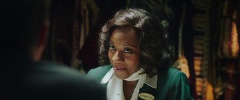 Movie still from “In Fabric” (2018), directed by Peter Strickland – An older woman with curly brown hair wearing a green jacket; Close Up shot, Over the shoulder angle