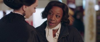 Movie still from “In Fabric” (2018), directed by Peter Strickland – A woman talking to another woman in front of a wall; Close Up shot, Over the shoulder angle