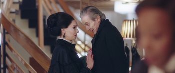 Movie still from “In Fabric” (2018), directed by Peter Strickland – An older man and a younger woman in black clothes; Close Up shot, Over the shoulder angle