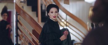 Movie still from “In Fabric” (2018), directed by Peter Strickland – A woman in a black dress and a black hat; Close Up shot, Over the shoulder angle