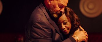 Movie still from “In Fabric” (2018), directed by Peter Strickland – A man and a woman embracing each other in front of a black background; Extreme Close Up shot, High angle
