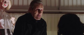 Movie still from “In Fabric” (2018), directed by Peter Strickland – An older man in a black shirt is looking at the camera; Close Up shot, Over the shoulder angle