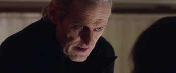 Movie still from “In Fabric” (2018), directed by Peter Strickland – An old man with a white beard and blue eyes looking at the camera; Close Up shot, Low angle