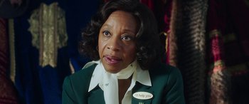 Movie still from “In Fabric” (2018), directed by Peter Strickland – An older black woman wearing a green jacket and a white neck tie; Close Up shot, Over the shoulder angle