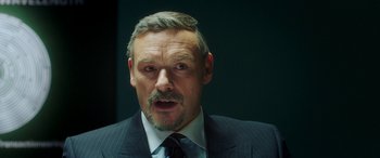 Movie still from “In Fabric” (2018), directed by Peter Strickland – A person wearing a suit and tie; Close Up shot, Over the shoulder angle