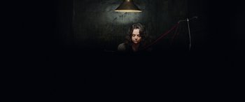 Movie still from “In Fabric” (2018), directed by Peter Strickland – A woman sitting at a desk in a dark room; Medium shot, Overhead angle