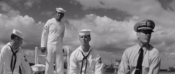 Movie still from “In Harm's Way” (1965), directed by Otto Preminger – A black - and - white photo of a sailor and two other sailors; Medium shot, Low angle