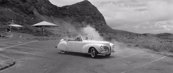 Movie still from “In Harm's Way” (1965), directed by Otto Preminger – An old car is driving down a road; Extreme Wide shot, Low angle