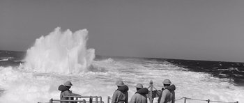Movie still from “In Harm's Way” (1965), directed by Otto Preminger – A black and white photo of a group of men standing in front of the ocean; Extreme Wide shot, High angle
