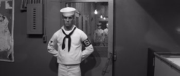 Movie still from “In Harm's Way” (1965), directed by Otto Preminger – A man in a sailor's uniform standing in front of a door; Medium shot, Low angle