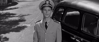 Movie still from “In Harm's Way” (1965), directed by Otto Preminger – A man in a uniform standing in front of a car; Medium shot, Low angle