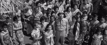 Movie still from “In Harm's Way” (1965), directed by Otto Preminger – A group of people standing around a man in uniform; Medium shot, High angle